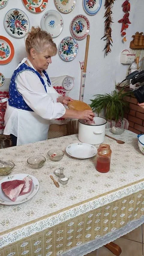 Matyó Mami főzés közben, matyó mellényben a konyhaasztalnál