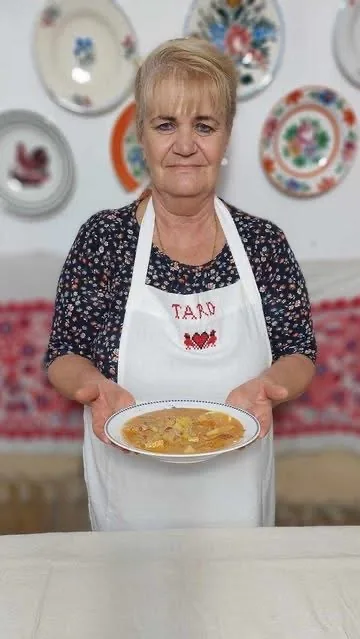 Császár Józsefné, Matyó Mami, egy tányér levest tart a tardi konyhában, matyó tányérokkal a falon